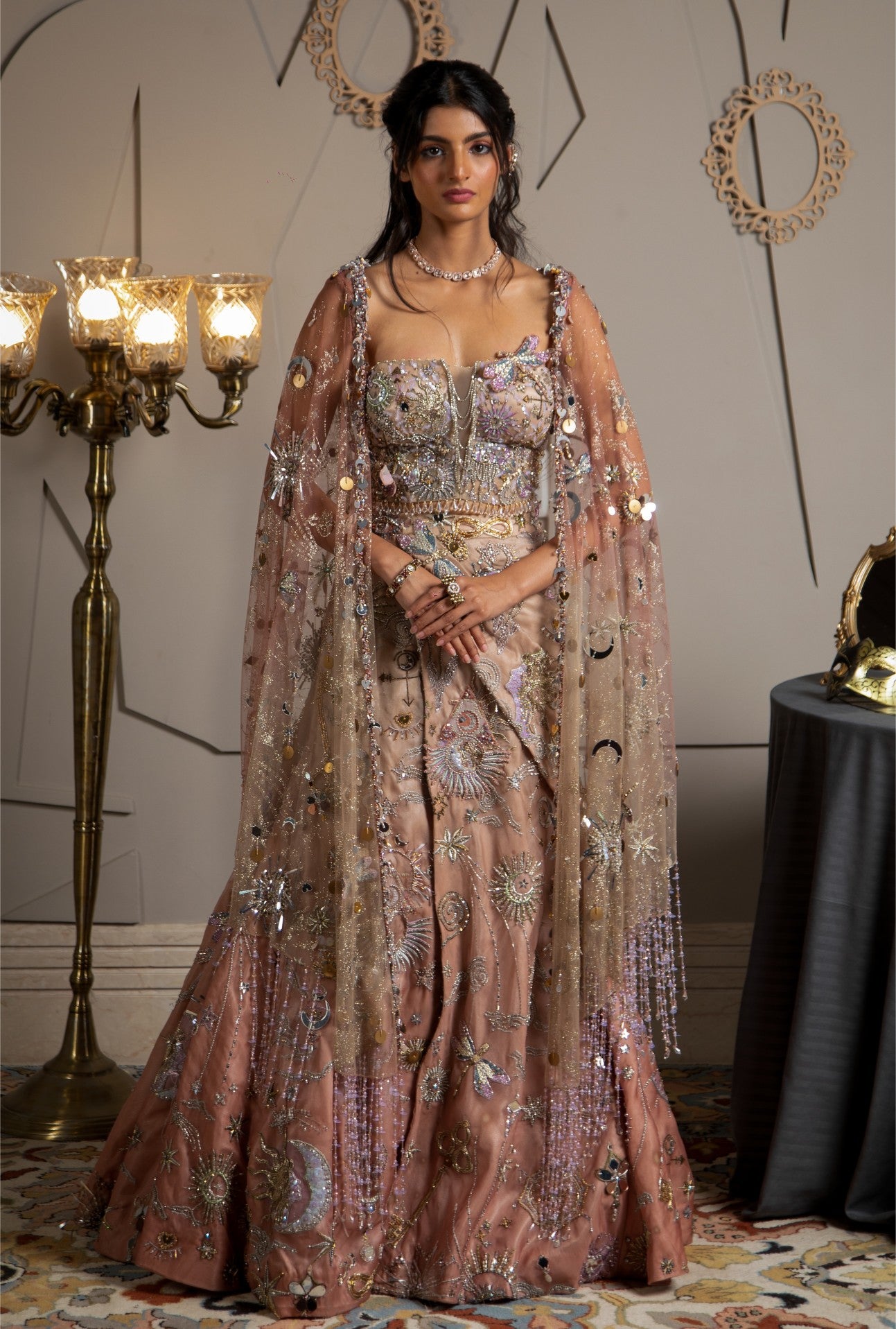 Woman in an ornate, embellished dress standing in a decorated room with chandeliers.